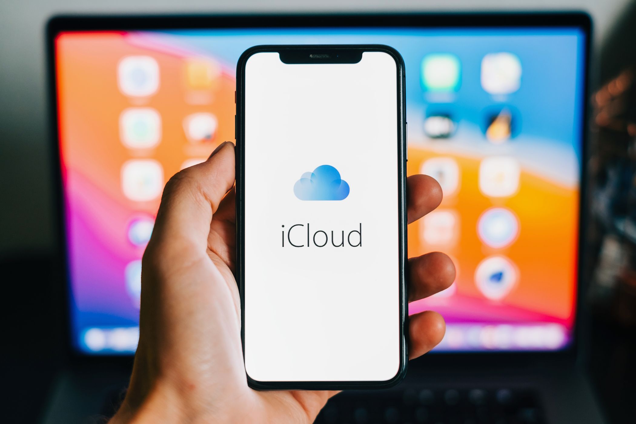 آرم iCloud که در آیفون با یک مک بوک در پس زمینه ظاهر می شود