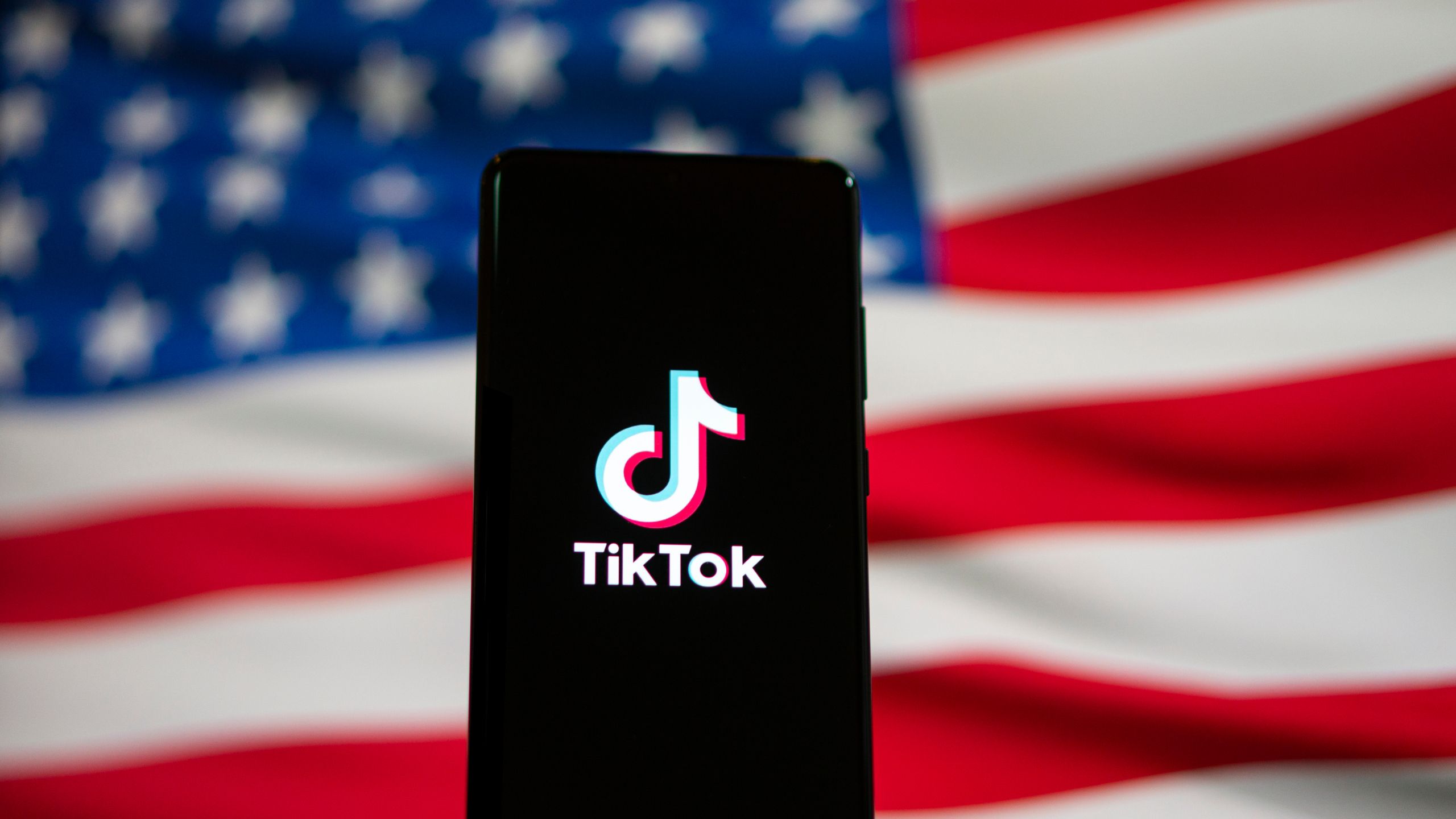آرم Tiktok از طریق تلفن در مقابل پرچم ایالات متحده