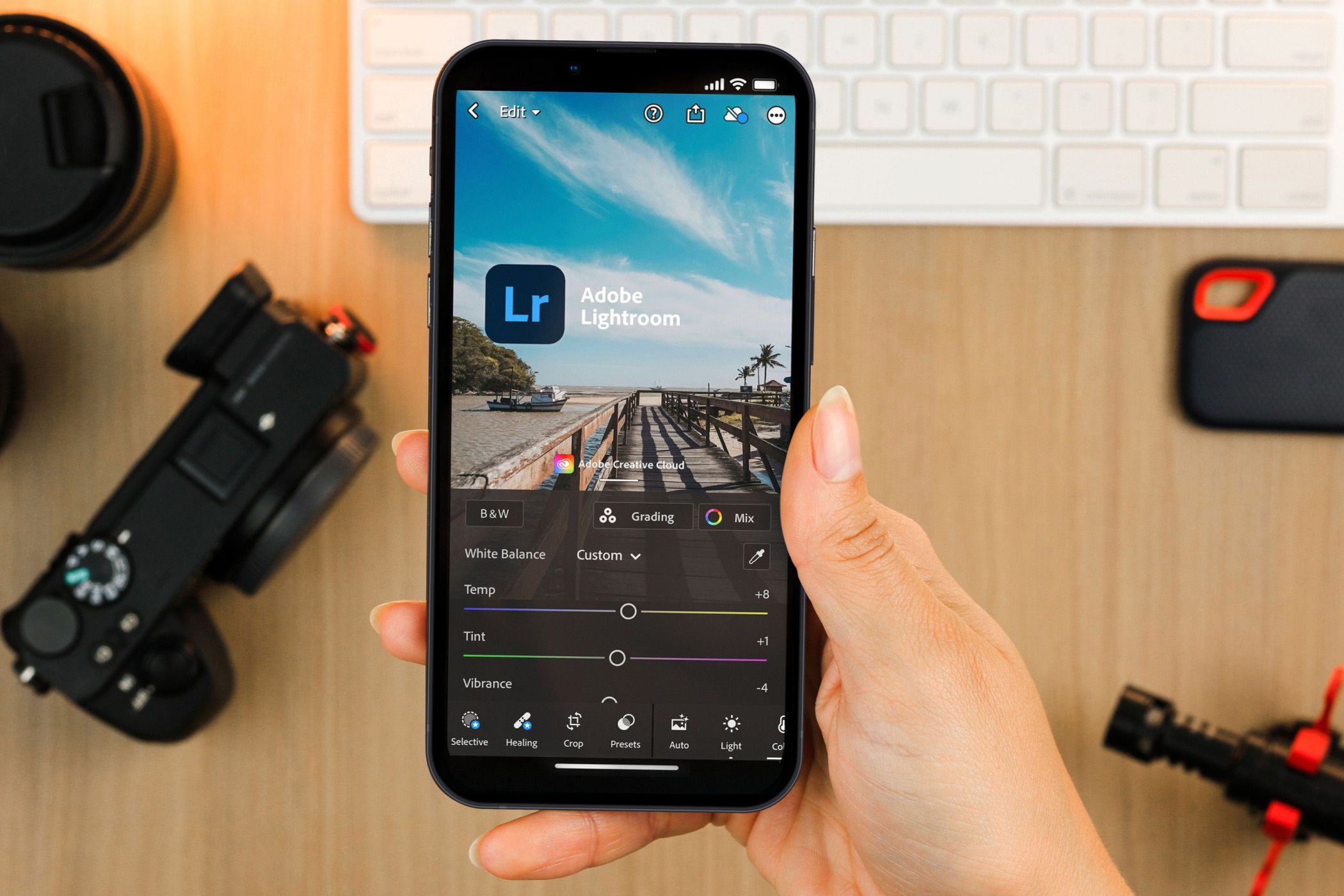 نگه داشتن تلفن هوشمند ، نمایش برنامه تلفن همراه Lightroom ، با تجهیزات دوربین در پس زمینه