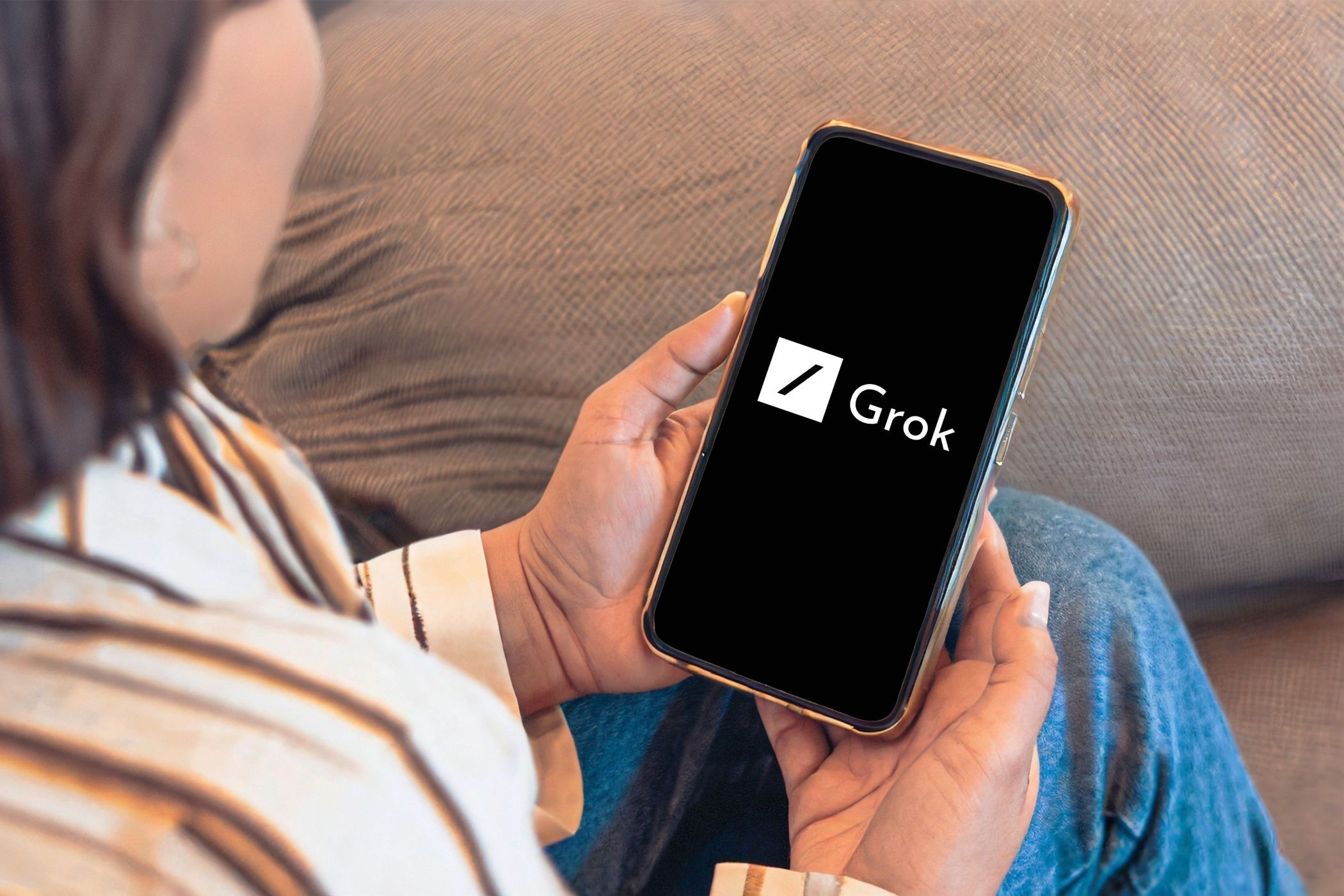شخصی که با آرم Grok AI به تلفن هوشمند نگاه می کند