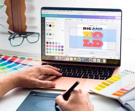 یک لپ‌تاپ با Canva باز بر روی میز همراه با برخی ابزارهای طراحی