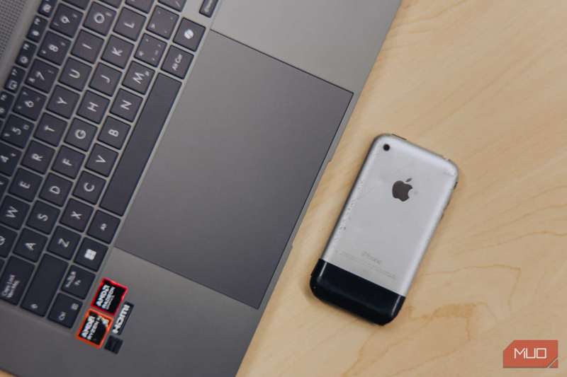 تصویر نزدیک ترک‌پد ASUS Zenbook S 16 کنار iPhone 2G