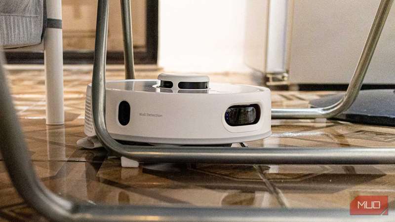 SwitchBot Mini Robot Vacuum K10+ Pro در حال شستشو بین پایه‌های صندلی‌های تاشو