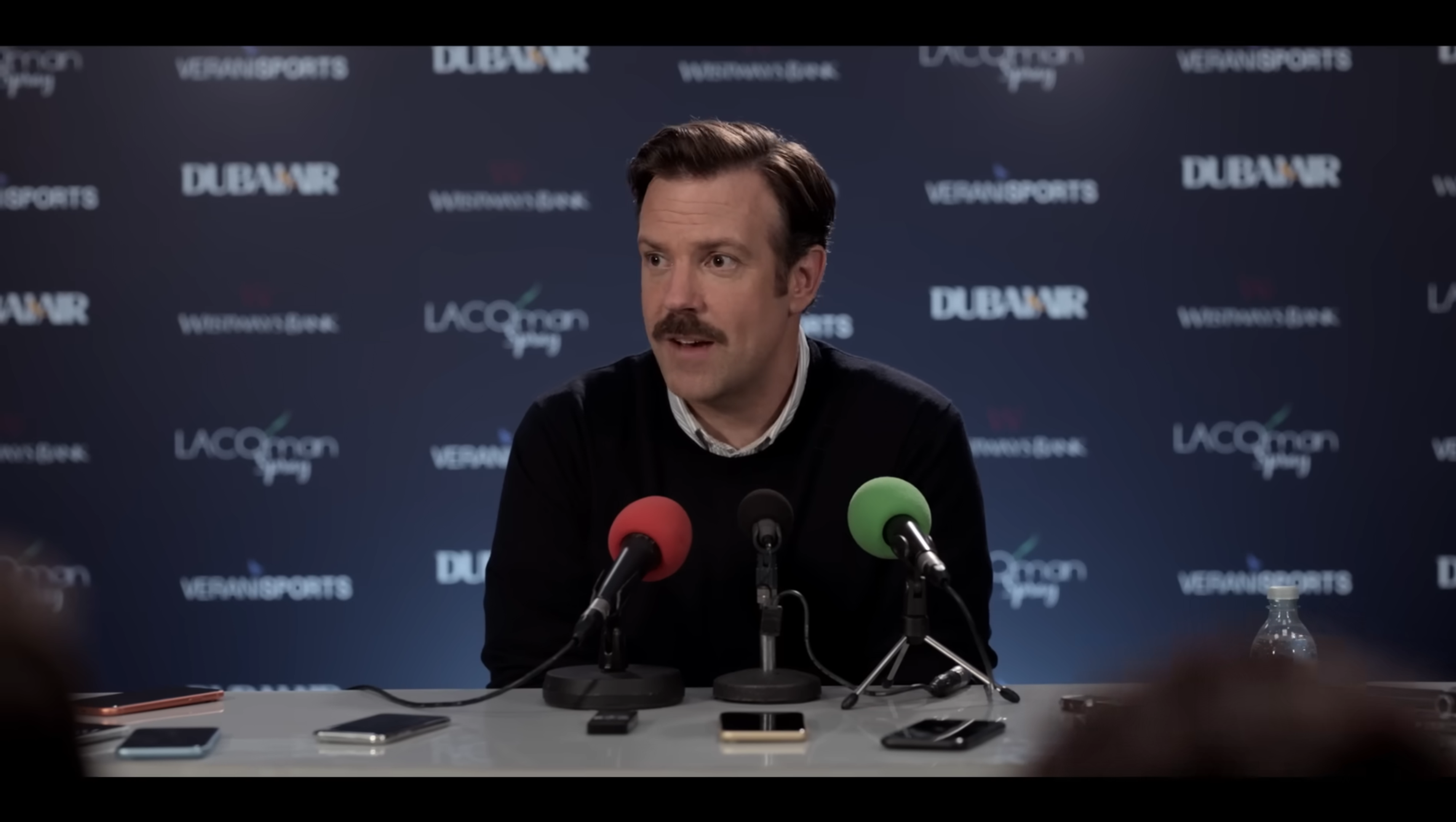جیسن سودیکیس از Ted Lasso که در یک کنفرانس مطبوعاتی می‌خندد