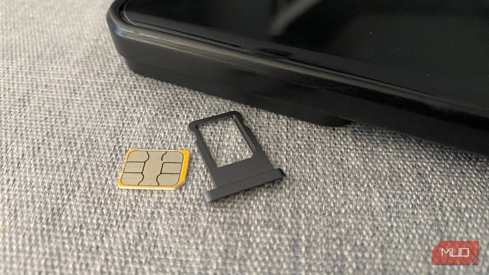 یک کارت SIM و نگهدارنده پلاستیکی کنار یک گوشی موبایل روی میز