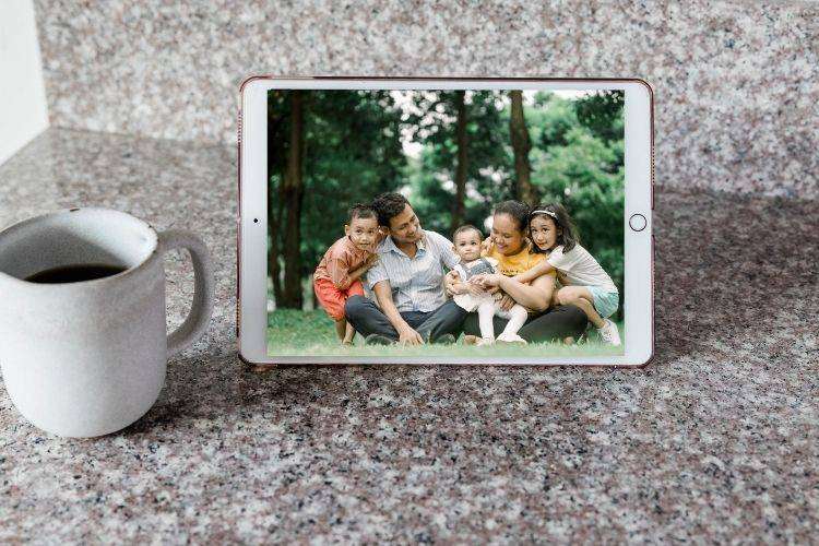 فنجان قهوه و تبلت که یک خانواده خوشحال را روی سطح مرمر نشان می‌دهد