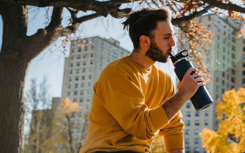 مرد جوانی که در پارک از بطری آب می‌نوشد