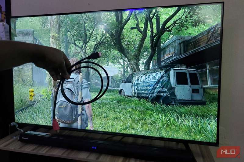 دست در حال نگه داشتن کابل HDMI در جلوی صفحه تلویزیون.