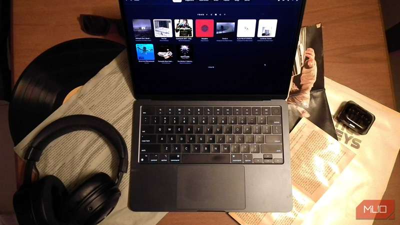 یک مک‌بوک که در یک میز پر از سی‌دی‌های موسیقی، یک صفحه‌ویولن و هدفون در حال پخش موسیقی است