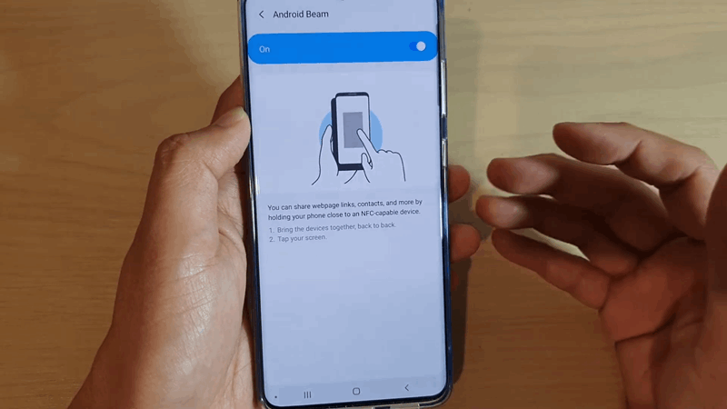 شخصی که یک گوشی هوشمند در دست دارد و صفحه تنظیمات فعال Android Beam را نمایش می‌دهد.
