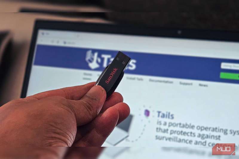 دست شخصی که یک درایو فلش Sandisk را در حال نگه‌داری دارد و یک لپ‌تاپ در پس‌زمینه