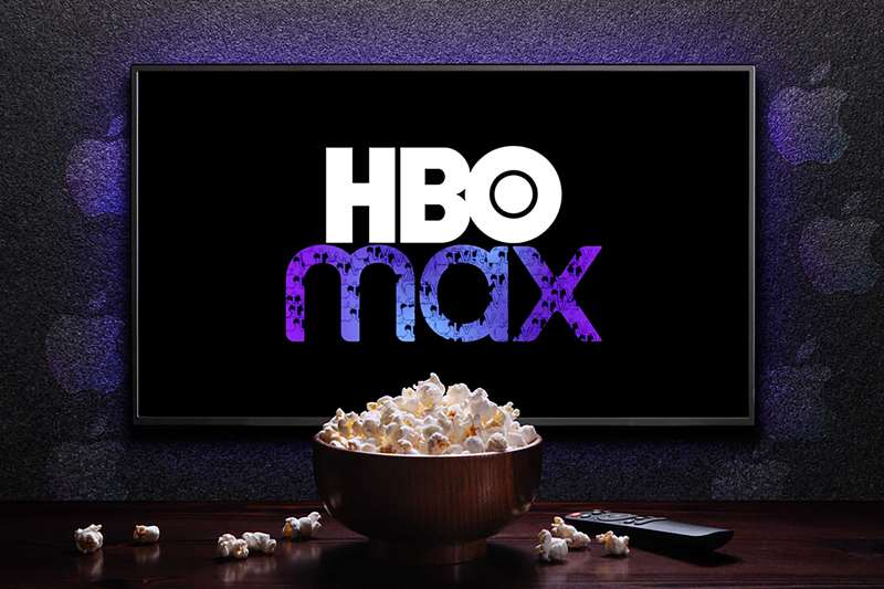 لوگوی HBO Max روی تلویزیون با کاسه پاپ‌کورن و ریموت کنترل روی میز و لوگوهای Apple TV پاشیده شده بر روی دیوار