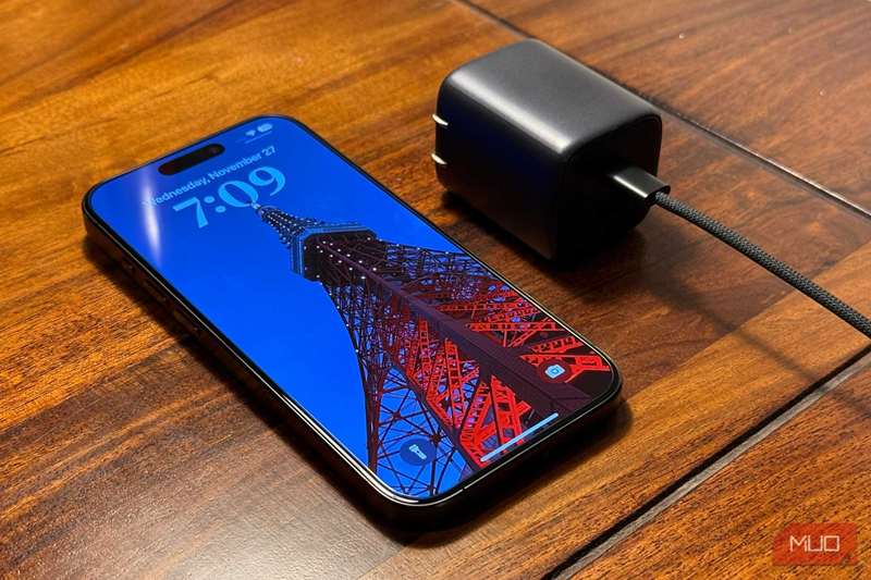 آیفون کنار یک آداپتور برق بر روی میز چوبی قرار گرفته