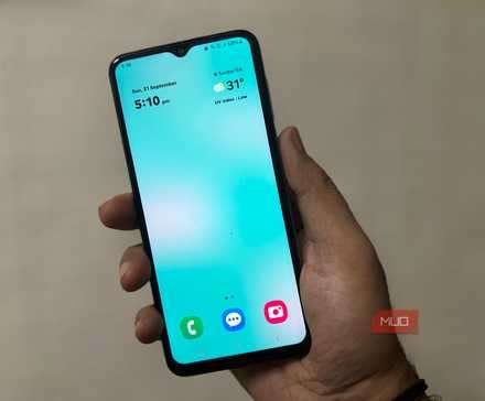 شخصی که گوشی سامسونگ را در دست دارد و صفحه اصلی تمیز با ساعت و آب‌وهوا را نشان می‌دهد