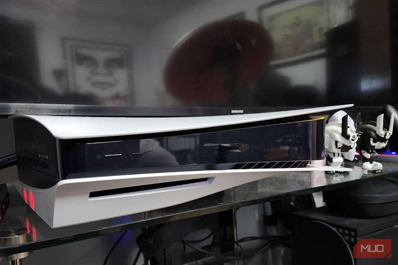 یک پلی‌استیشن 5 زیر یک تلویزیون هوشمند روی یک مرکز سرگرمی شیشه‌ای قرار گرفته