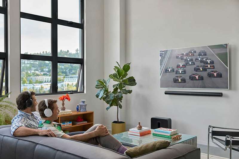 دو مرد روی یک کاناپه تلویزیون نگاه می‌کنند، هر دو هدفون‌های Sonos Ace به‌سر دارند.