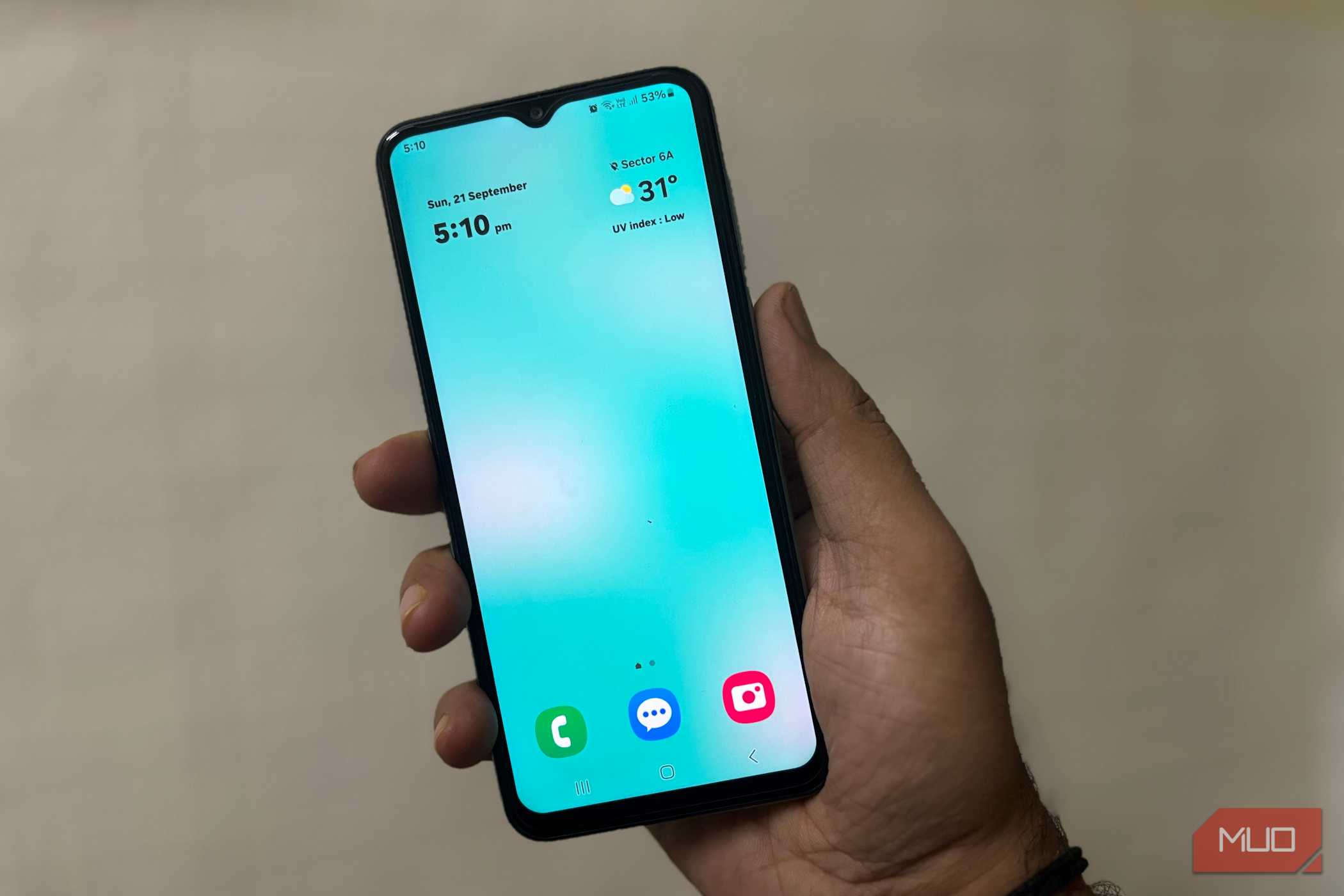 شخصی که گوشی سامسونگ را در دست دارد و صفحهٔ اصلی تمیز با ساعت و آب و هوا را نشان میدهد