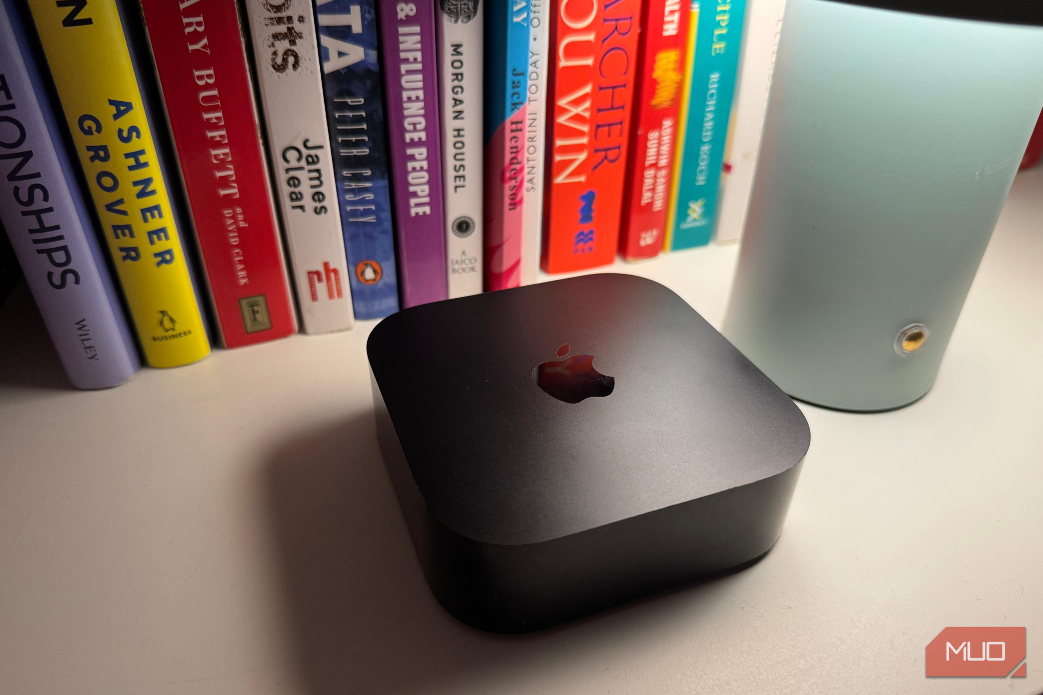 Apple TV در کنار یک لامپ با چند کتاب در پس‌زمینه