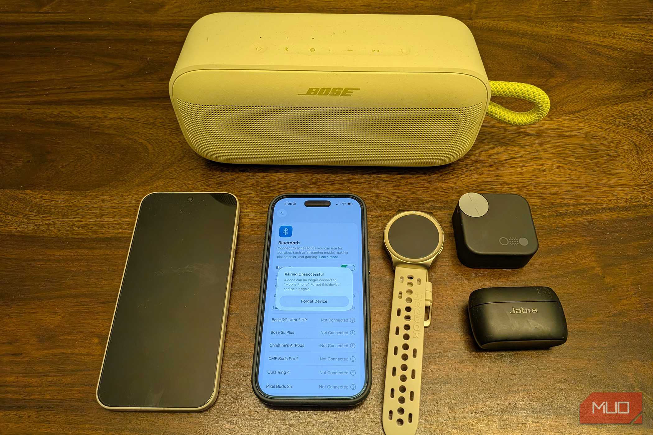 دو تلفن، دو کیس هدفون بی‌سیم، یک اسپیکر بلوتوث، و یک ساعت هوشمند روی میز