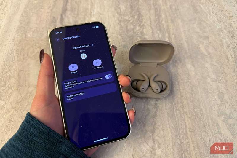 هدفون‌های Powerbeats Fit در کیف خود کنار دستی که گوشی Google Pixel را می‌گیرد