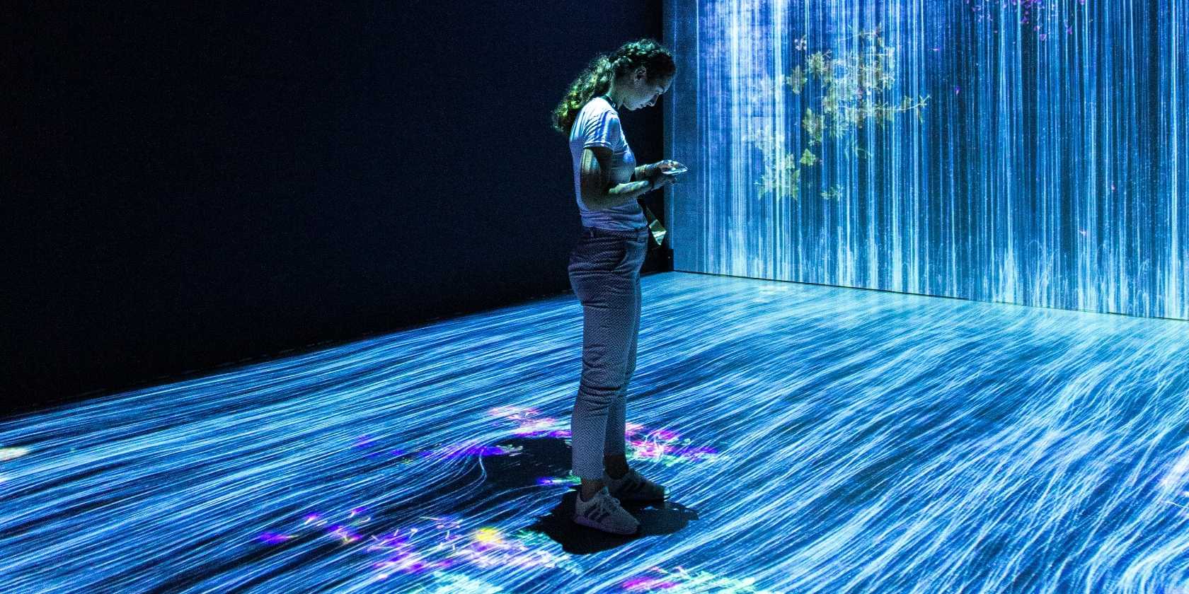 زن ایستاده و به گوشی هوشمند خود نگاه می‌کند.