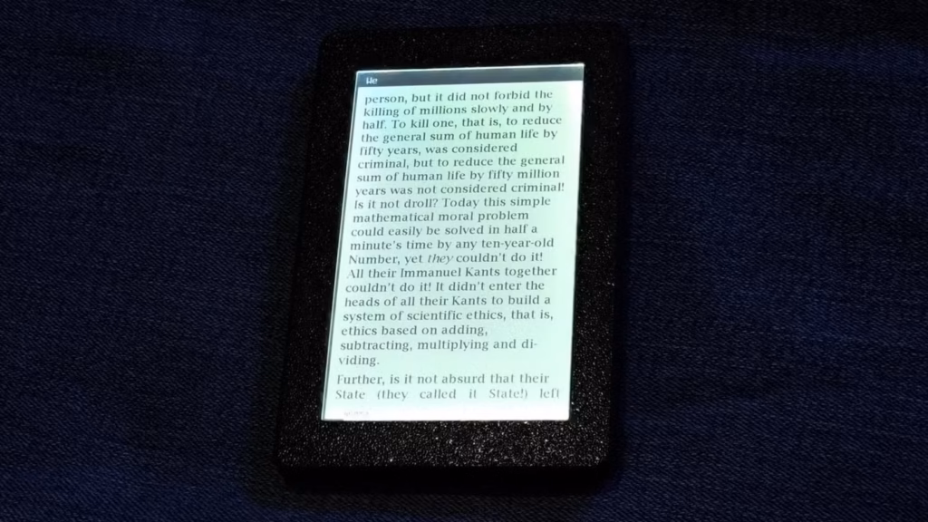 نمای نزدیک کتاب خوان Open Book Touch که صفحه ای از یک کتاب الکترونیکی را در قاب مشکی بافت دار روی زمینه پارچه ای آبی تیره نمایش می دهد.