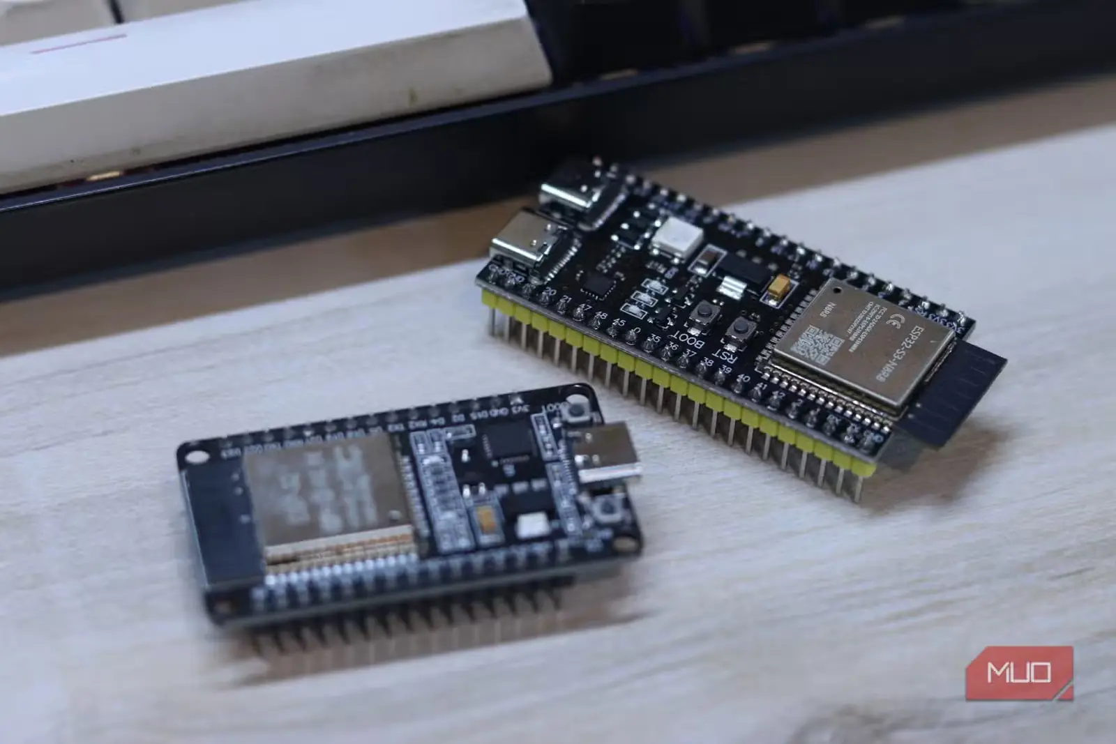 دو برد ESP32، کلاسیک و S3، کنار هم روی میز چوبی