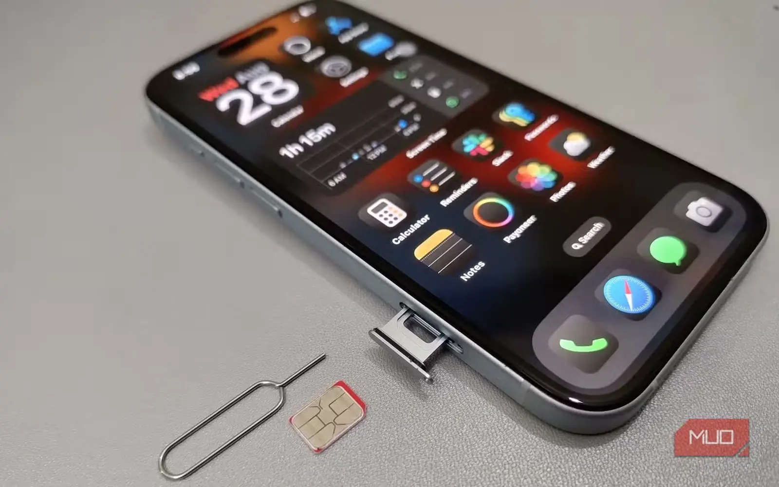 گوشی iPhone 15 در کنار سینی سیمکارت و ابزار بیرونآوردن آن روی میز
