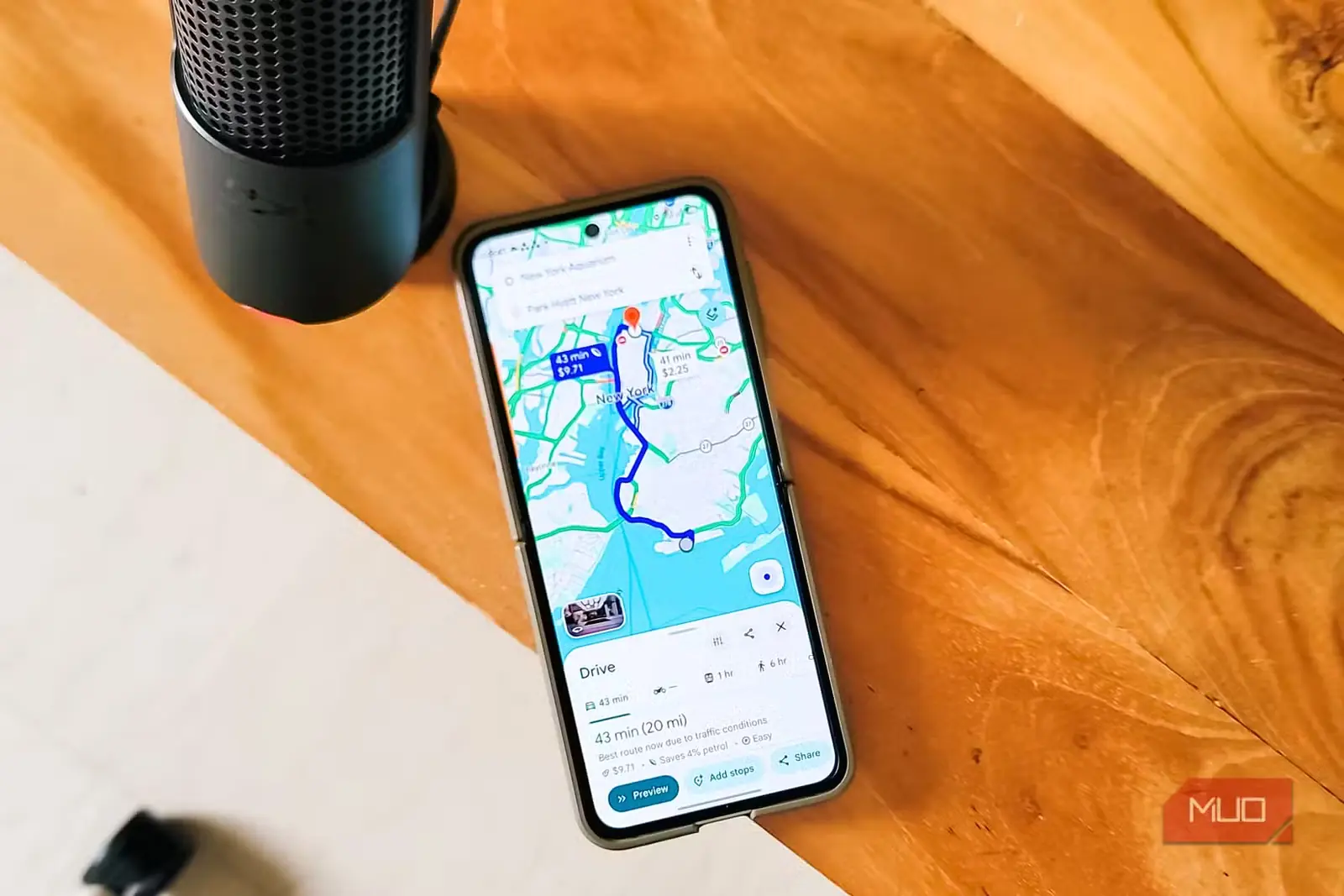 گوشی هوشمند روی میز چوبی با مسیریابی Google Maps در نیویورک و میکروفون