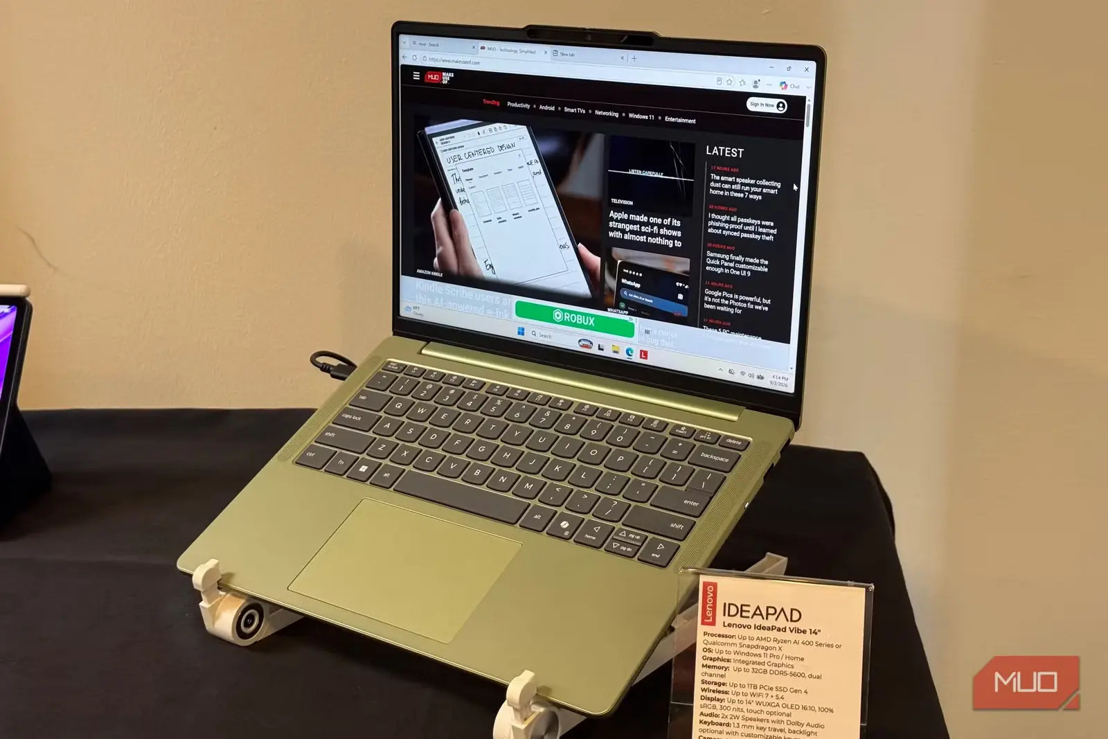 دستگاه سبزرنگ Lenovo IdeaPad Vibe 14 روی پایه، کنار کارت مشخصات آن در میز نمایش