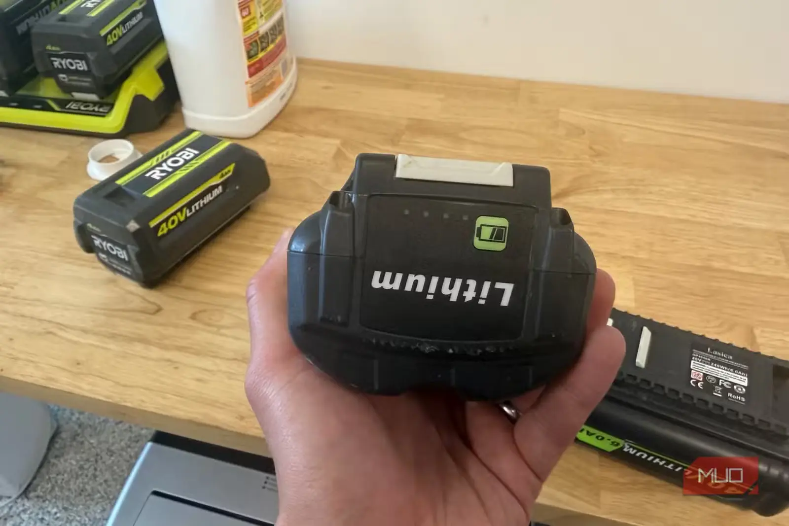 دستی در حال نگهداشتن باتری متفرقه 40V سازگار با Ryobi، با باتری اصل Ryobi در پسزمینه