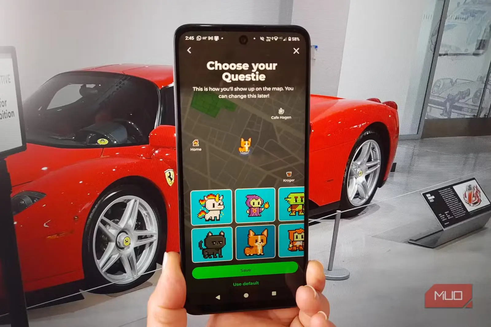 دستی در حال نگهداشتن گوشی با صفحه انتخاب چهرک Questie در MapQuest و یک Ferrari قرمز در پسزمینه