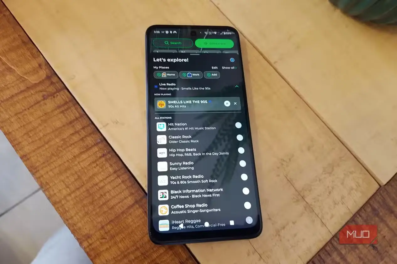 گوشی هوشمند روی میز چوبی با قابلیت Live Radio در MapQuest؛ رادیوی «بوی دهه ۹۰ میدهد» بالای فهرست ایستگاههای در دسترس در حال پخش است